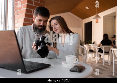 Colleagues photographers working in cafe using camera and laptop, viewing pictures on camera. New modern technologies concept Stock Photo