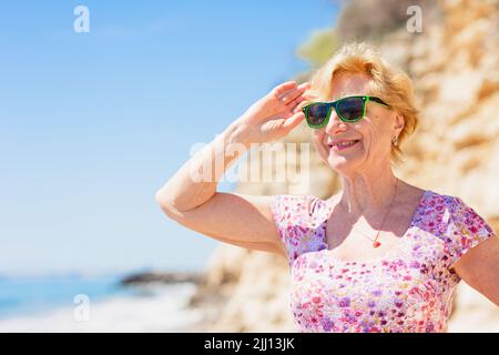 Elderly woman in sunglasses looking at the sea and having fan. Stock Photo