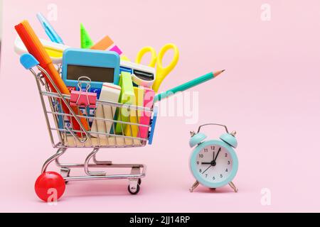 Blue shopping cart or trolley and stationery pen pencil clip pin rubber isolated on pink background. Online shopping concept for school Stock Photo