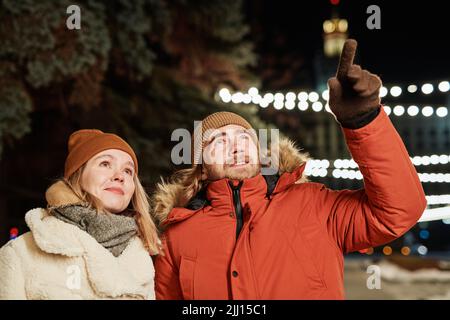 Horizontal shot of young couple walking on winter evening, man showing something to his girlfriend Stock Photo