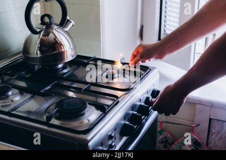 A man's hand with a match lights a gas burner or a gas stove in the kitchen. Stock Photo