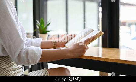 Pretty young Asian woman relaxes reading a book or novel in the comfortable modern coffee shop. cropped image Stock Photo