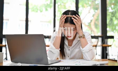 Stressed millennial Asian businesswoman or office employee feeling tried, upset on her work performance, having a depression syndrome. Stock Photo