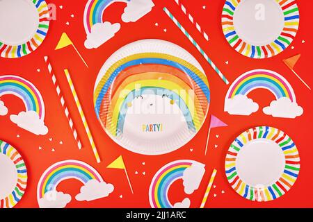 Party flat lay with colorful plates, rainbow napkins and drinking straws on red background Stock Photo