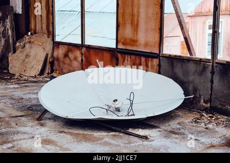 Old white satellite dish in an abandoned warehouse.  Stock Photo