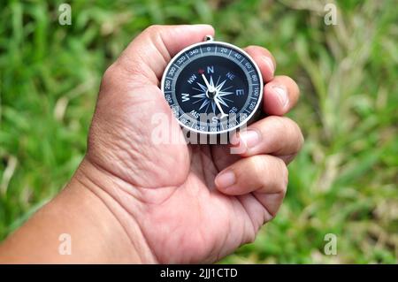 Holding navigation compass close up green leaves background Stock Photo