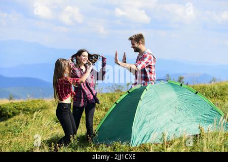 Well done. Good job. Teamwork concept. Hiking activity. Friends set up tent on top mountain. Camping equipment. Weekend in mountains. Man and girls Stock Photo