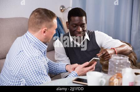 Two smiling male friends with smartphones and talking Stock Photo