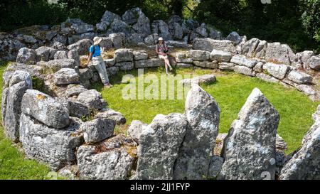 21st century visitors resting on the Iron-age foundations of  a hut-circle at Din Lligwy, Moelfre, Anglesey, Wales, UK Stock Photo