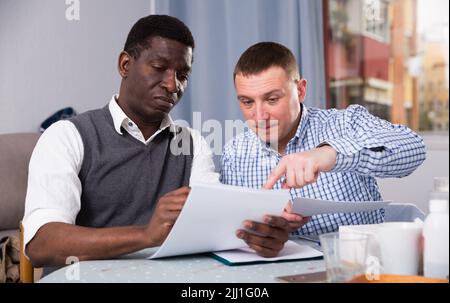 Serious man wit friend discussing documents at home Stock Photo