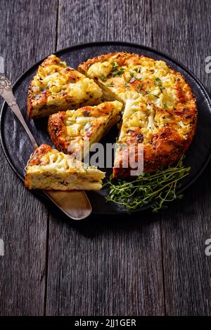 Cauliflower Cake with Pecorino Romano cheese, Basil and spices sliced on black platter on dark wooden table with a slice on cake shovel, vertical view Stock Photo