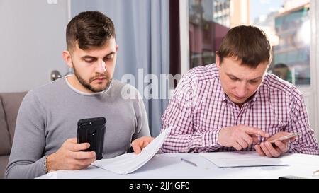 Serious males with documents and phone at home table Stock Photo