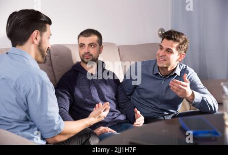 Three males having fun talking on couch Stock Photo