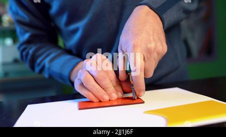 Man cuts with glass cutter details of future mural or stained glass window. Craftsman works with colored glass in fusing technique in workshop. Hobby Stock Photo