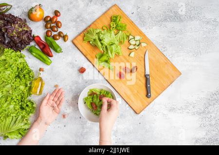 Woman adding salt in vegetable salad bowl. Health eating concept. Stock Photo