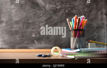 School supplies on wooden table and blackboard in the background. Front view. Horizontal composition. Stock Photo