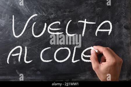Hand writing vuelta al cole on blackboard with chalk. Front view. Horizontal composition. Stock Photo