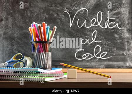 School supplies on wooden table and blackboard in the background and message vuelta al cole. Front view. Horizontal composition. Stock Photo