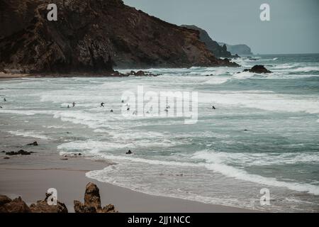 The beautiful beach of Praia do Amado on the western Algarve on an overcast day. Groups of surfers fill the rough ocean Stock Photo