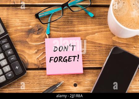 A desk with 'don't forget' text on pink paper surrounded by calculator, smartphone and glasses Stock Photo