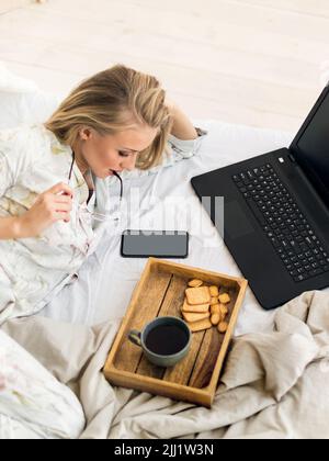 Young woman checking news in her smartphone in bed. Freelancer morning. Vertical photo. Stock Photo