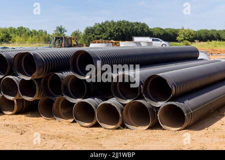 In order to build a drain system on a construction site, PVC new black plastic pipes are stacked in rows Stock Photo