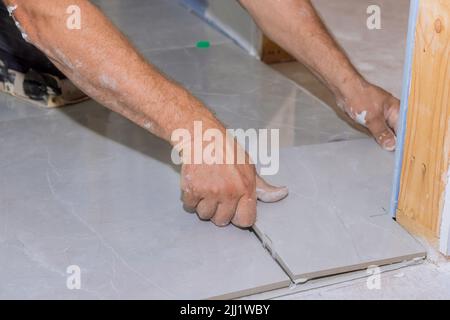 With the help of a home construction worker, placing ceramic tile on an adhesive surface Stock Photo