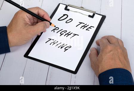 Hand with pencil writing the words Do The Right Thing on a paper with black clipboard to remind you an important task or appointment. Stock Photo
