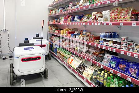 Moscow, Russia, March 2022: Two delivery robots for parcels and goods are charging from an outlet in post office next to shelves with food. Express pa Stock Photo