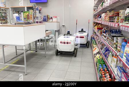 Moscow, Russia, March 2022: Two delivery robots for parcels and goods are charging from an outlet in post office next to shelves with food. Express pa Stock Photo