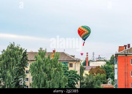 Colorful balloons fly in the sky above the roofs of high-rise buildings in a provincial city Stock Photo