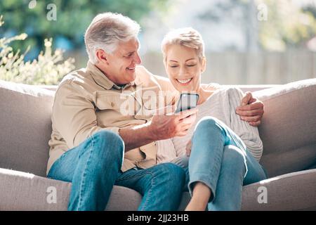 Care to share. a happy senior couple using a smartphone on the sofa at home. Stock Photo