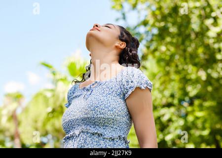 Young caucasian woman wearing a blue floral summer dress standing on city park, outdoors breathing fresh air. Concept of healthy lifestyle. Stock Photo