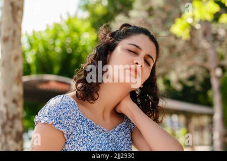 Beautiful brunette woman wearing summer dress standing on city park, outdoors feeling hurt joint shoulder back pain ache, fibromyalgia concept, close Stock Photo