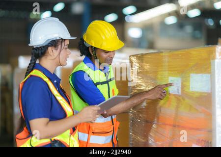 Asian couple warehouse workers checking shipment status on digital tablet computer prepare for delivery to customer. Employees teamwork. Stock Photo