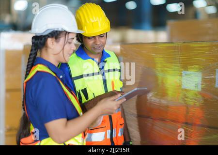 Asian couple warehouse workers checking shipment status on digital tablet computer prepare for delivery to customer. Employees teamwork. Stock Photo