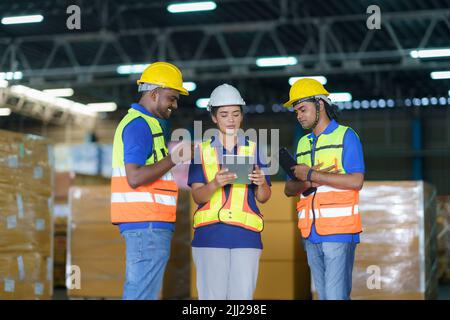 Asian team warehouse workers checking shipment status on digital tablet computer prepare for delivery to customer. Employees teamwork. Stock Photo