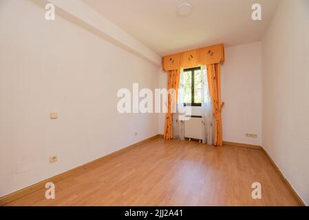 Empty room with oak hardwood floor, white painted walls and matching millwork and window with yellow curtains Stock Photo
