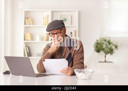 Elderly man looking at a document and sitting in front of a laptop computer at home Stock Photo
