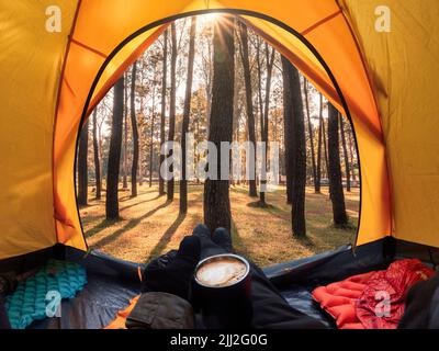Traveler holding coffee relaxing inside a orange tent and enjoy the view of sunset on pine forest in national park Stock Photo