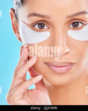 Keeping my skin looking young. Studio portrait of an attractive young woman wearing under eye patches against a blue background. Stock Photo