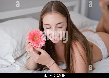 Calm woman with flower lying on her bed. morning routine. successful date. bright white bedroom. Stock Photo
