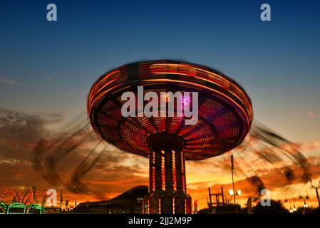 COSTA MESA, CALIFORNIA - 20 JUL 2022: Carnival ride with motion blur at the Orange County Fair with a beautiful sunset sky. Stock Photo