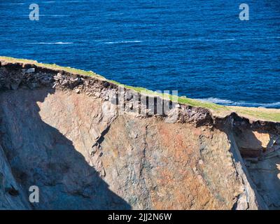 Eroding soil, subsoil and bedrock shown on sheer cliffs near Uyea in Northmavine, Shetland, UK. Taken on a sunny day with the sea in the background. Stock Photo