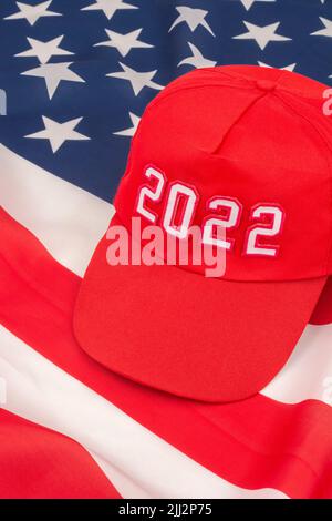 Red MAGA-type cap with 2022 date and US Stars and Stripes flag. For November 2022 US Midterm elections & US Republican Red Wave wipe-out of Democrats. Stock Photo