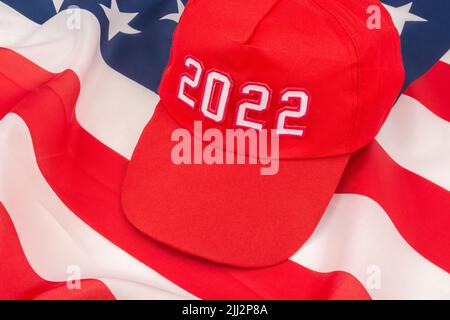 Red MAGA-type cap with 2022 date and US Stars and Stripes flag. For November 2022 US Midterm elections & US Republican Red Wave wipe-out of Democrats. Stock Photo
