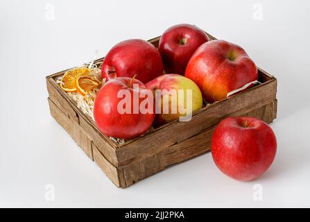 apples in a decorative box lined with wood shavings on a white background at close range, ripe fruit and slices of dried oranges Stock Photo