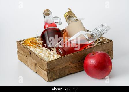 bottles with liquors in a small decorative box lined with shavings on a white background, a red apple and dried orange slices Stock Photo