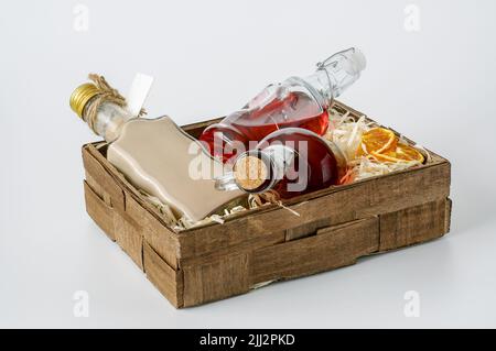 bottles with liquors in a small decorative box lined with shavings on a white background, a red apple and dried orange slices Stock Photo