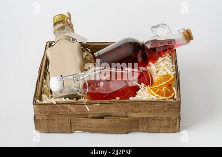 bottles with liquors in a small decorative box lined with shavings on a white background, a red apple and dried orange slices Stock Photo